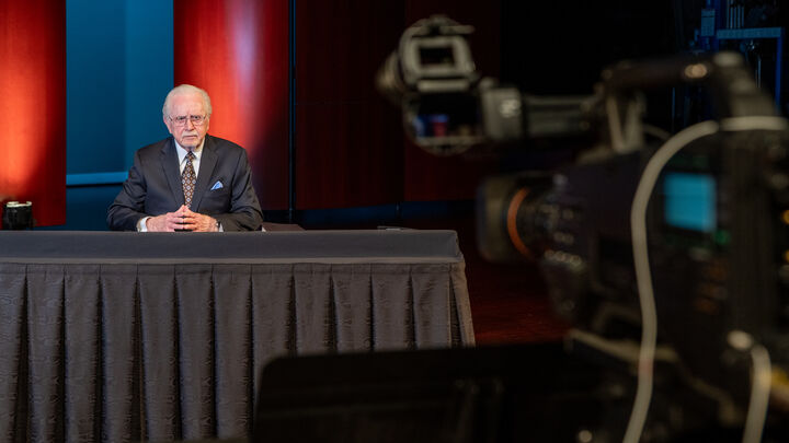 Gerald Flurry at a desk on a stage, a television camera in the foreground