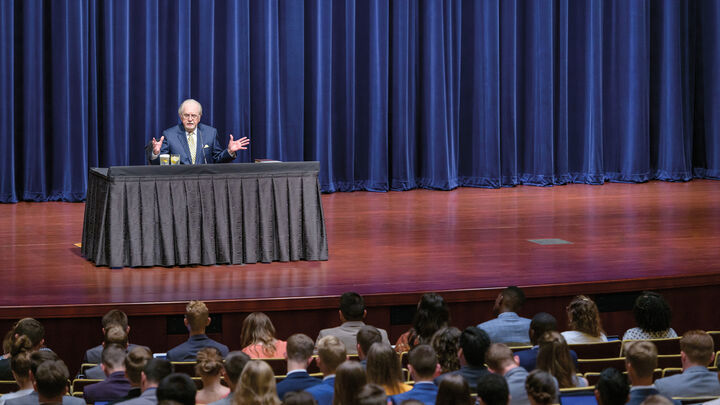 Gerald Flurry speaks from a desk on a stage to an audience of students