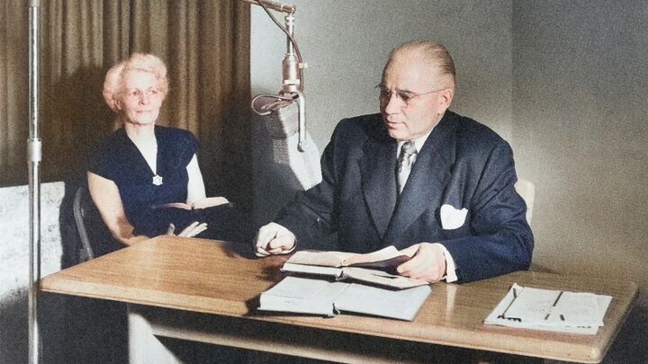 Herbert W. Armstrong at a desk before a studio microphone, his wife seated beside him