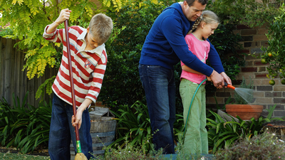 Boy (10-12) sweeping, twin sister and father watering garden with hose