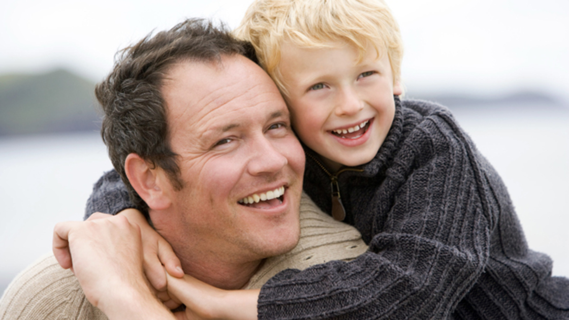 Father and son on a beach smiling 