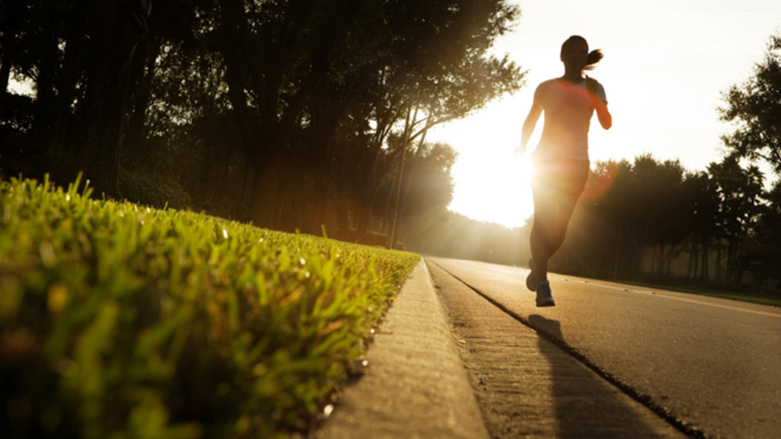 Photo of young woman running on rural road at sunrise.