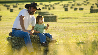 Father and daughter sitting on hay in a field