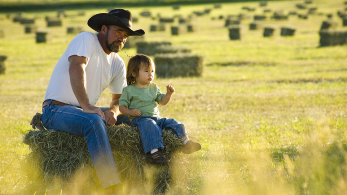 Father and daughter sitting on hay in a field