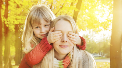 Younger sister standing behind older, covering her eyes