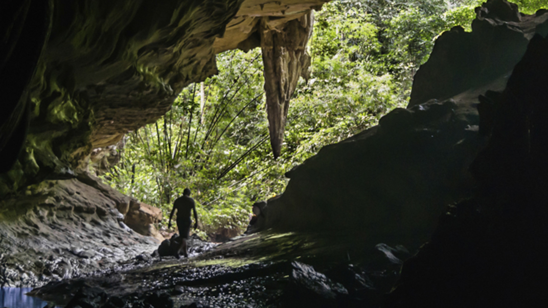Wide view from inside a huge cave with a man going out.
