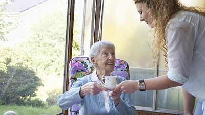 Caregiver serving a cup of coffee to 90 year old senior woman.