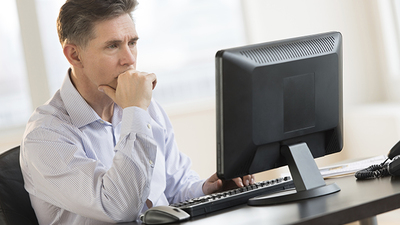 Mature businessman with hand on chin working on Desktop PC in office