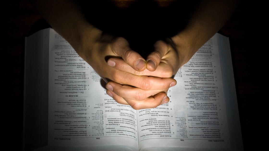 16x9 (Discretion)
The man's combined hands praying on the bible isolated in a black background