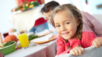 Portrait of happy girl sitting at festive table and looking at camera