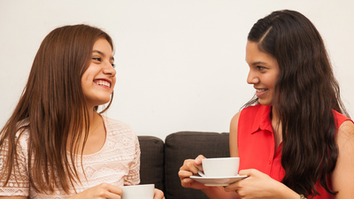 Beautiful Hispanic teenager having some coffee with her friend at home