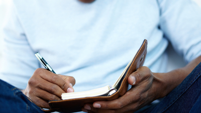 Close-up of young African man writing something in notepad