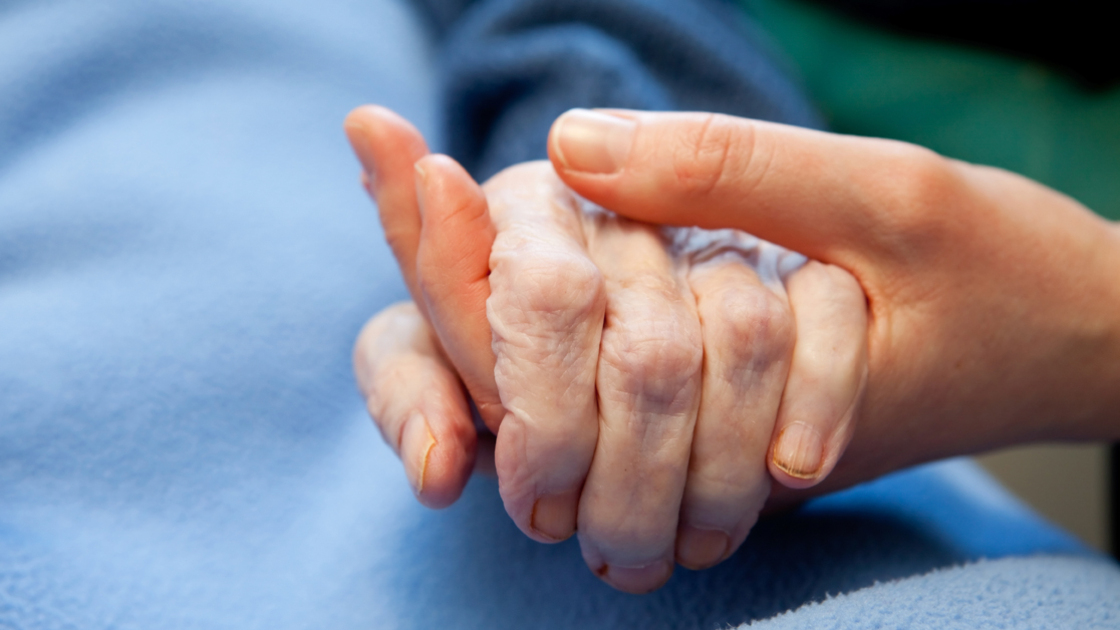 A young hand touches and holds an old wrinkled hand