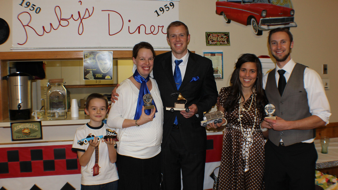 Winners pose with their most creative pine cars in front of “Ruby's Diner,” a cafeteria window transformed for the 1950s theme. From left: Seven Fuller, Mrs. Chelsey Weeks, Mr. David Weeks, Lauren Fehr, Kenneth Fehr.