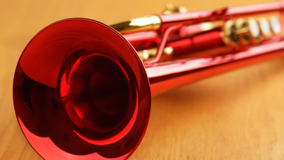 16x9(Lessons from a Doc)
A shining red trumpet with brass details. Trumpet is lying on wooden table with bell toward viewer. Close up of bell with shallow focus.