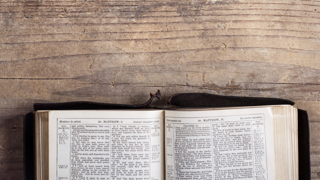 16x9(What is the Bible rated?)
Opened bible on a wooden desk background.