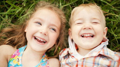 Top view portrait of two happy smiling kids lying on green grass. Cheerful brother and sister laughing together.