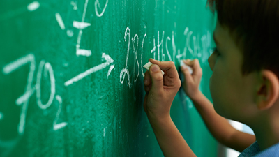 Schoolboy writing chemical equation on blackboard