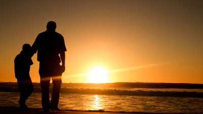 Father and son strolling on a beach during sunrise.