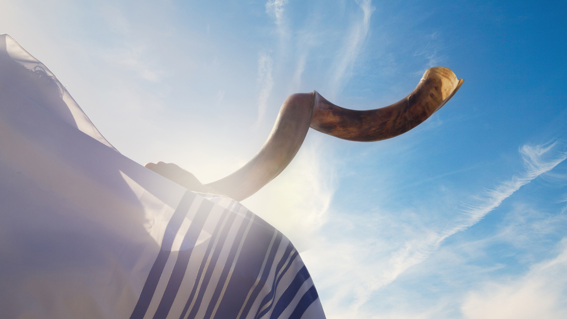 Jewish man blowing the Shofar against blue sky