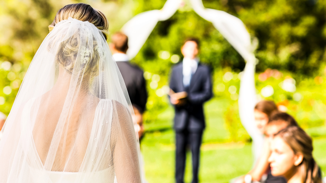 Rear view of bride wearing veil walking down the aisle during garden wedding. Horizontal shot.