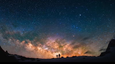 Silhouttes of the people standing together holding hands against the Milky Way in the mountains.