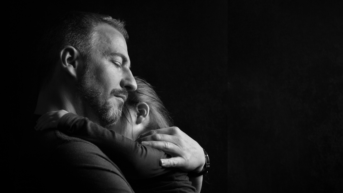 Touching Heart Felt Black and White Image of Father with Eyes Closed Hugging Young Daughter Tenderly with Dark Background with Copy Space