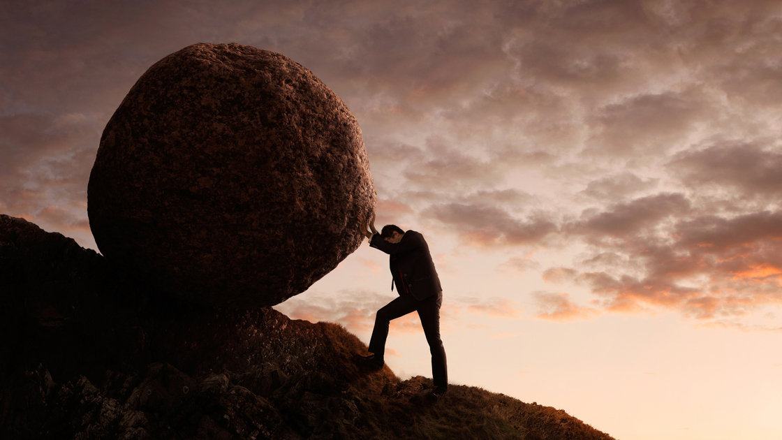 Silhouette of young businessman pushing large stone uphill with copy space