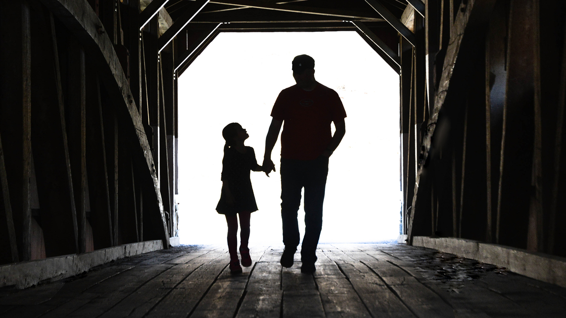 Father and daughter walking across a covered bridge holding hands. 