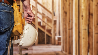 Photo of a construction worker with a white hard hat in one hand, closeup crop.