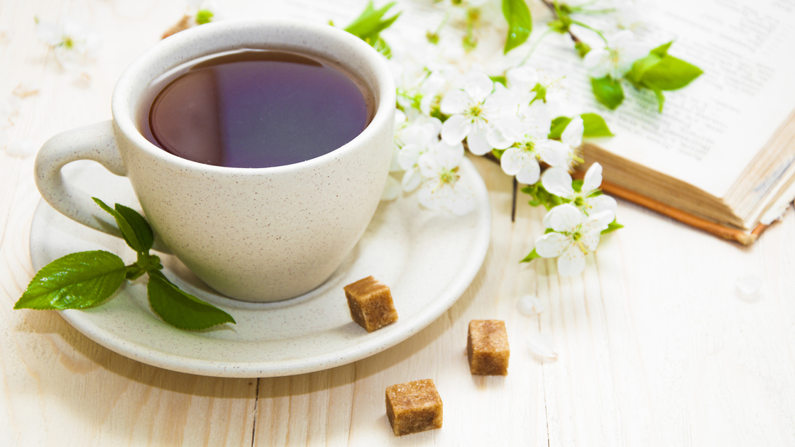 A cup of tea with spring flower cherry blossom and old book on a wooden background