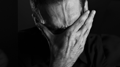 Close up of miserable man burying face in hans, looking desperate, isolated on black background.