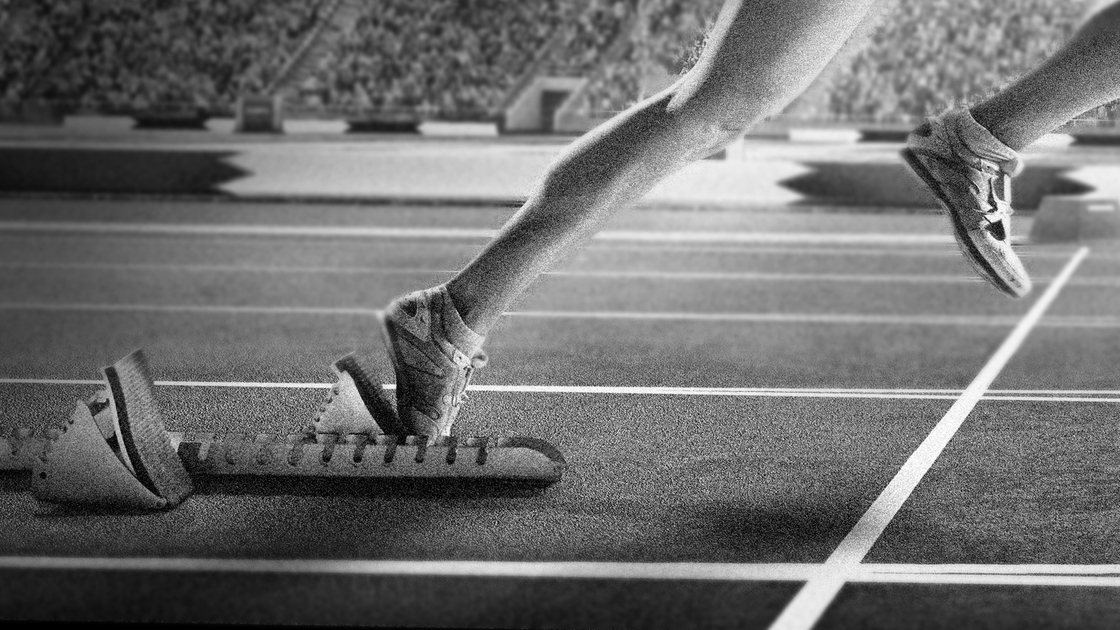 Professional female athlete sprinting from blocks on numbered start line on outdoor athletics track on olympic stadium full of spectators under a dramatic evening sky. Sprinter is wearing generic athletics kit.