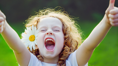 Laughing girl with daisy in her hairs, showing thumbs up.