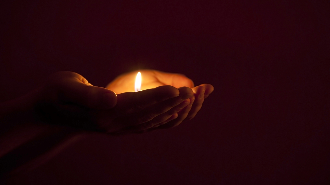 burning candle in human hands in darkness