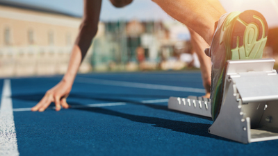 Feet on starting block ready for a spring start.  Focus on leg of a athlete about to start a race in stadium with sun flare.