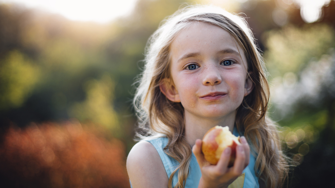 Little girl eating an apple. She is outdoors and looking at the camera, with apple juice on her face.