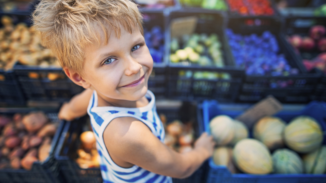 Happy little boy buying local groceries food at the tuscanian farmer's market at Cecina. Italy, Tuscany.