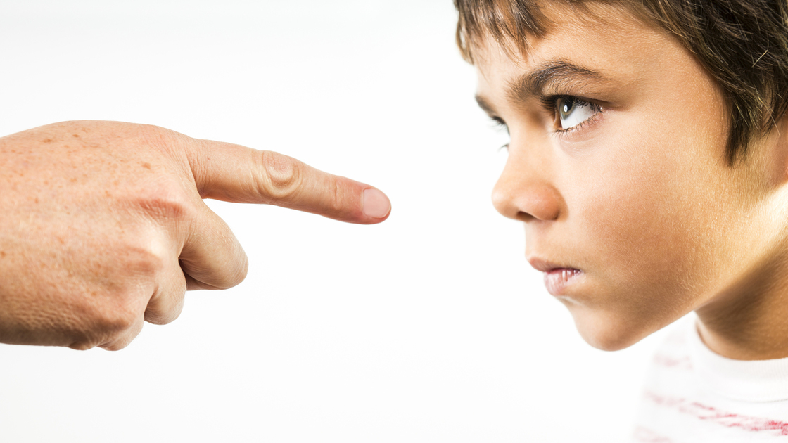 A photograph of a little boy being disciplined.  An angry child stares back in anger and defiance as he is being disciplined.  The finger of an adult is pointing directly at him.  