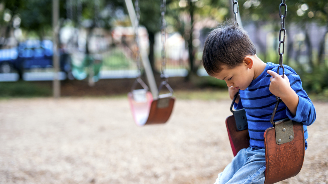 Young boy sitting on swings alone looking sad