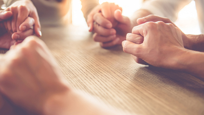 Cropped image of beautiful business team holding hands and praying while sitting in office