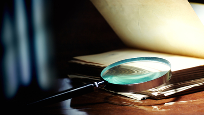 Old book and magnifier glass on a dark background as a symbol of knowledge and science