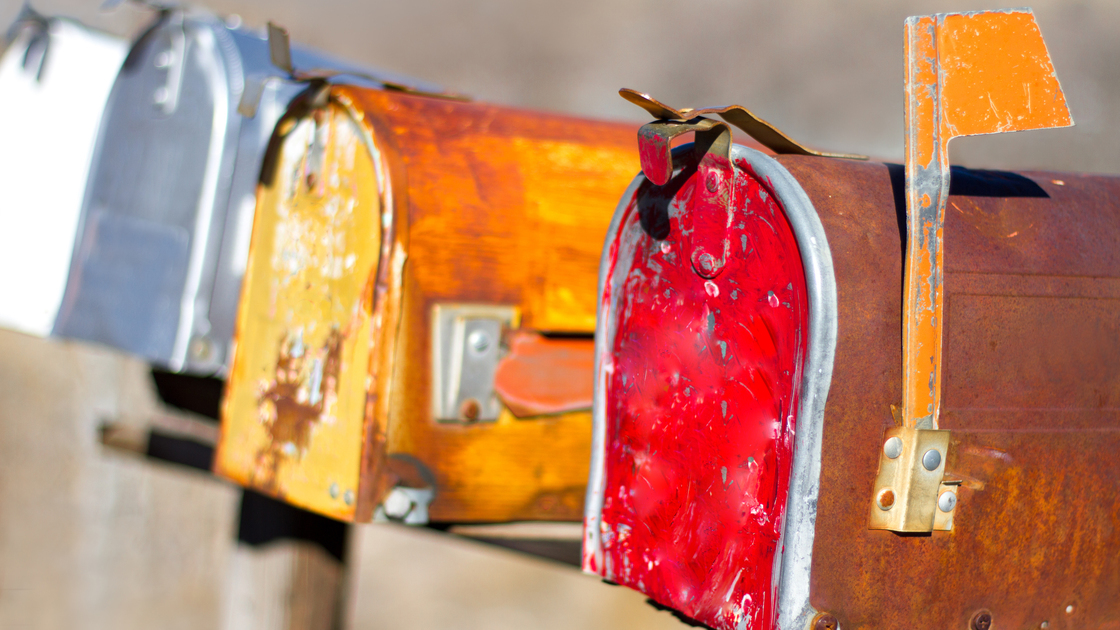 Row of colorful distressed rural mailboxes, one with a flag up. Sliver of copy space available at the top of the frame.