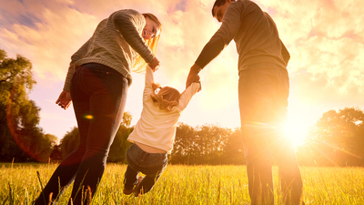 Happy family in the park evening light. The lights of a sun. Mom, dad and baby happy walk at sunset. The concept of a happy family.Parents hold the baby's hands.