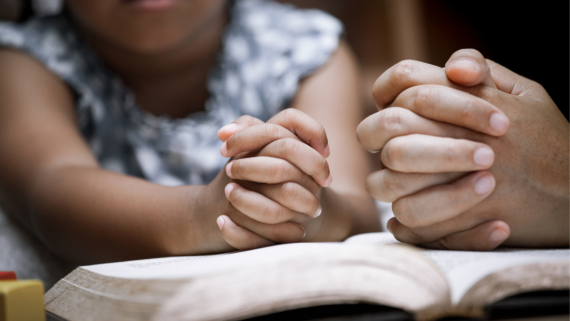 Mother and little girl hands folded in prayer on a Holy Bible together  for faith concept in vintage color tone