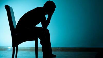 Depressed young man sitting on chair with face in his hands