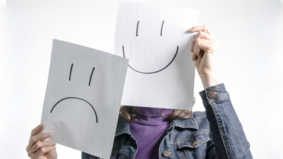 Woman holding paper with smiley and sad faces in front of her head, studio shot with white background