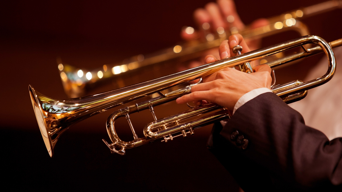 Hands of man playing the trumpet in the orchestra in dark colors 