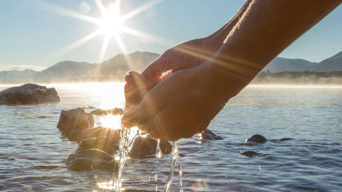 Human hand cupped to catch the fresh water from the lake, sunlight from sunrise passing through the transparence of the water.