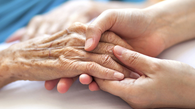 Woman holding senior woman's hand on bed